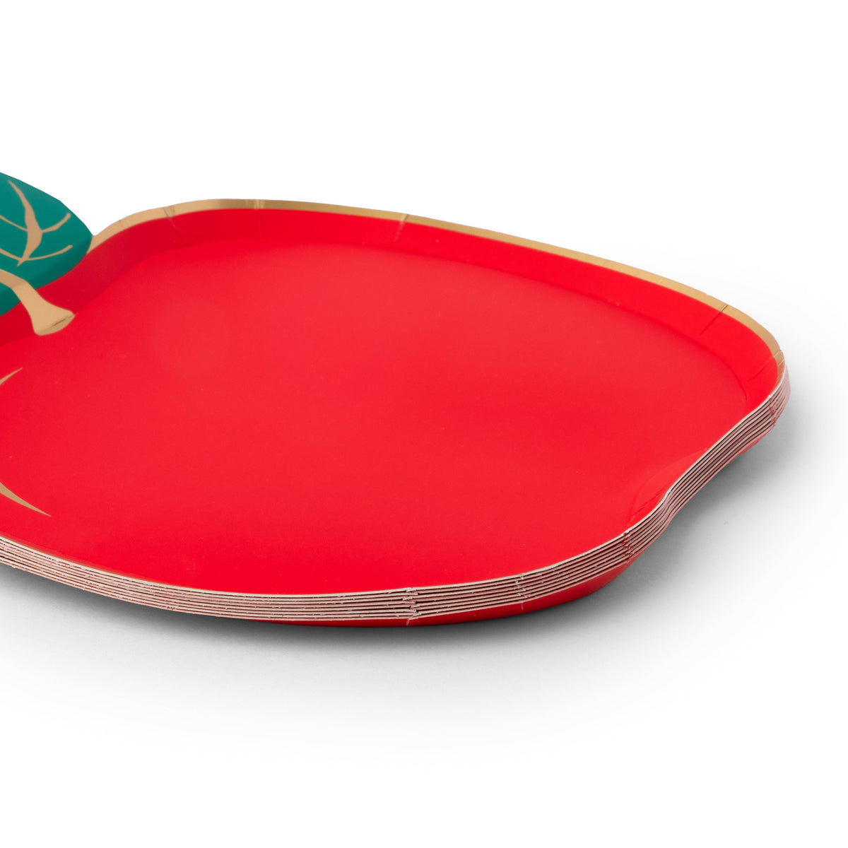 Close-up side view of stack of red apple shaped paper plates showing the apple silhouette, green leaf detail, gold foil edge, and paper construction