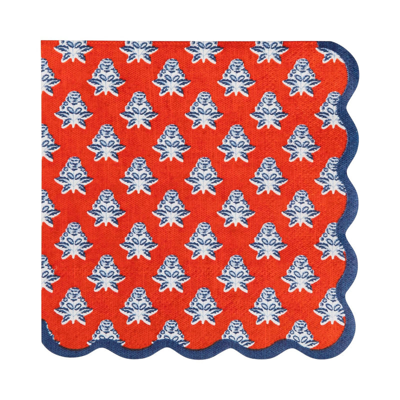 Single red block-print floral paper cocktail napkin showing indigo blue floral motif, red base, and navy scalloped edge on white background
