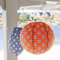 Red block print floral paper lantern and navy star paper lantern hanging from white porch beam with lake view behind