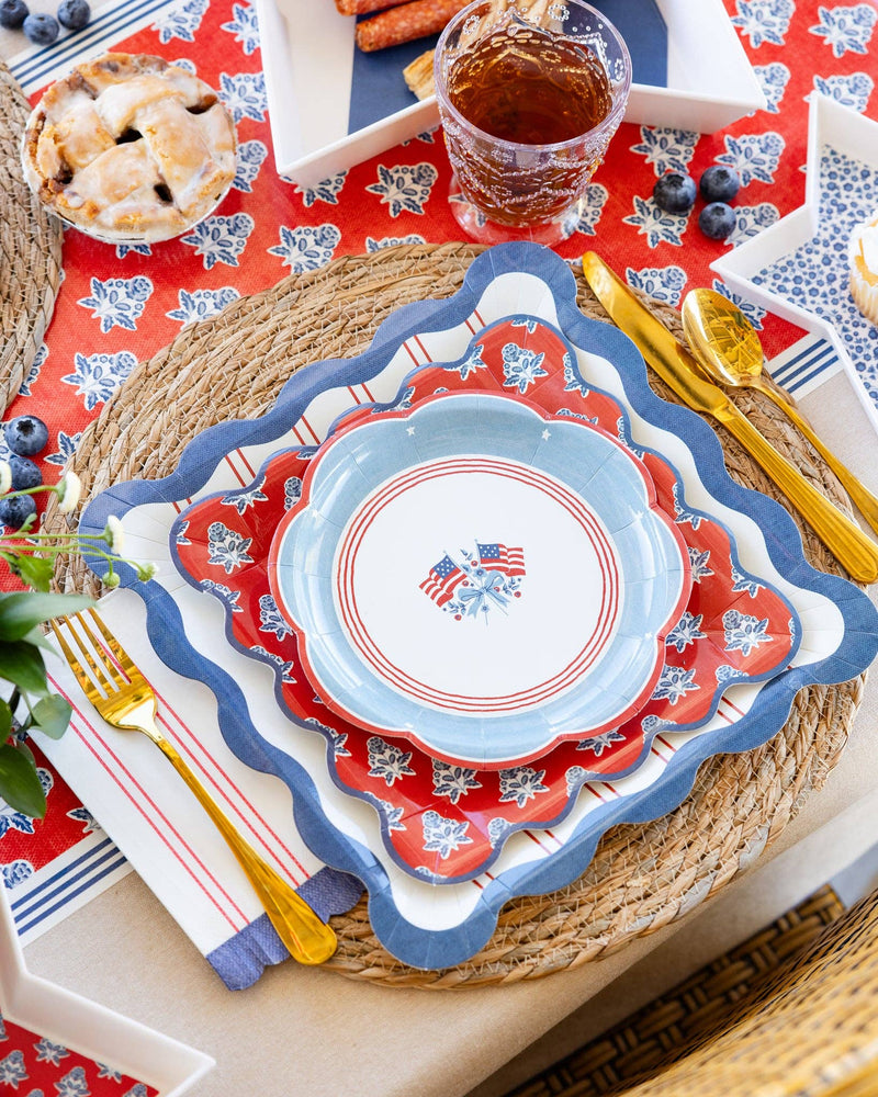 red block print floral scalloped paper plates styled in a layered 4th of July tablescape with American flag plates, red striped plates, gold flatware, and summer entertaining decor
