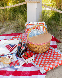 Beach picnic scene with red block print floral table runner in wicker basket alongside Americana paper plates and strawberries