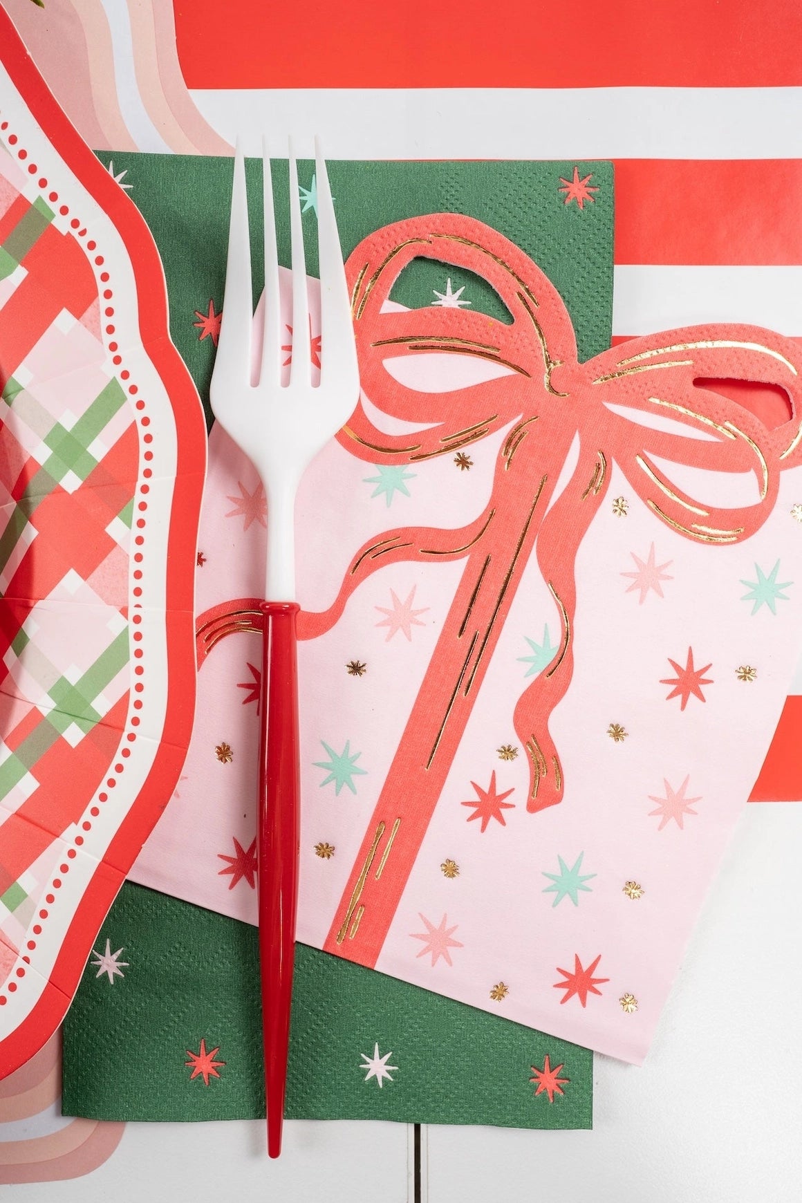 Close-up angled view of a white and red fork resting on the pink vintage present napkin layered over a green paper napkin.