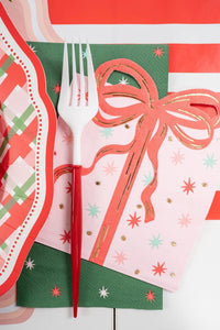 Close-up angled view of a white and red fork resting on the pink vintage present napkin layered over a green paper napkin.