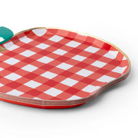 Angled close-up of a stack of red gingham apple shaped paper plates with gold foil trim and a green leaf detail.