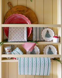 Red gingham scalloped paper napkins draped over Christmas tree paper plates on a cream kitchen shelf with fresh greenery