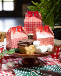 Red gingham treat box on a wood cake stand with s'mores and chocolate.