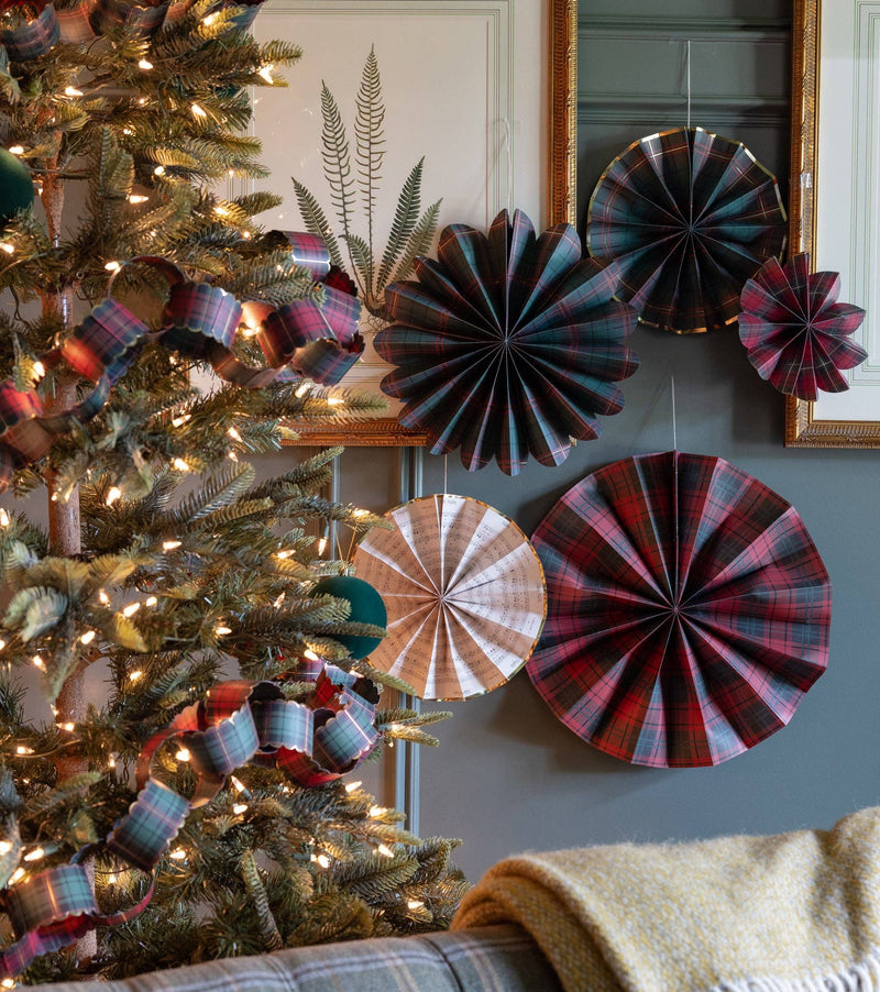 Red and green plaid Christmas paper fans styled on a wall by a Christmas tree