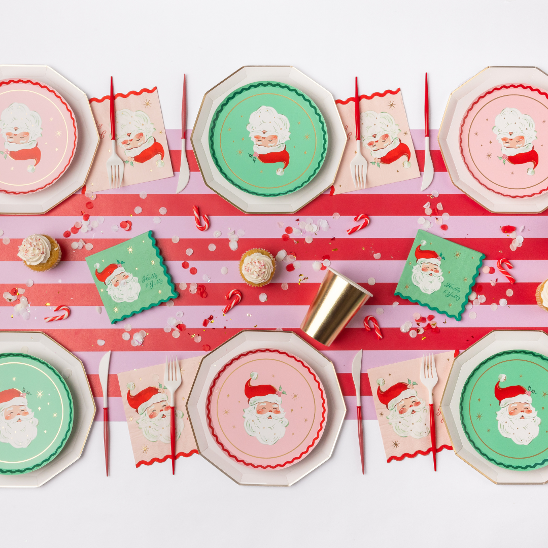 Red-and-green Christmas tablescape with green and pink Santa plates, the Santa napkins, gold cups, and a striped candy-cane runner.