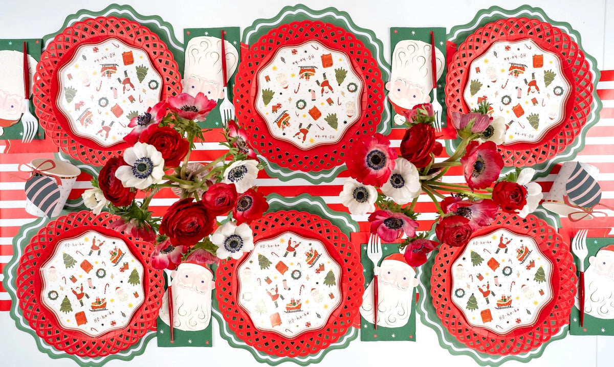 Overhead with red lattice chargers, icon plates, Santa napkins, green star guest towels, and red anemones.