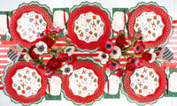Overhead with red lattice chargers, icon plates, Santa napkins, green star guest towels, and red anemones.