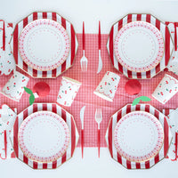 Cherry party table setting with red and white cabana stripe dinner plates, pink gingham plates, cherry print cups, and scalloped cherry napkins on a red grid table cover.