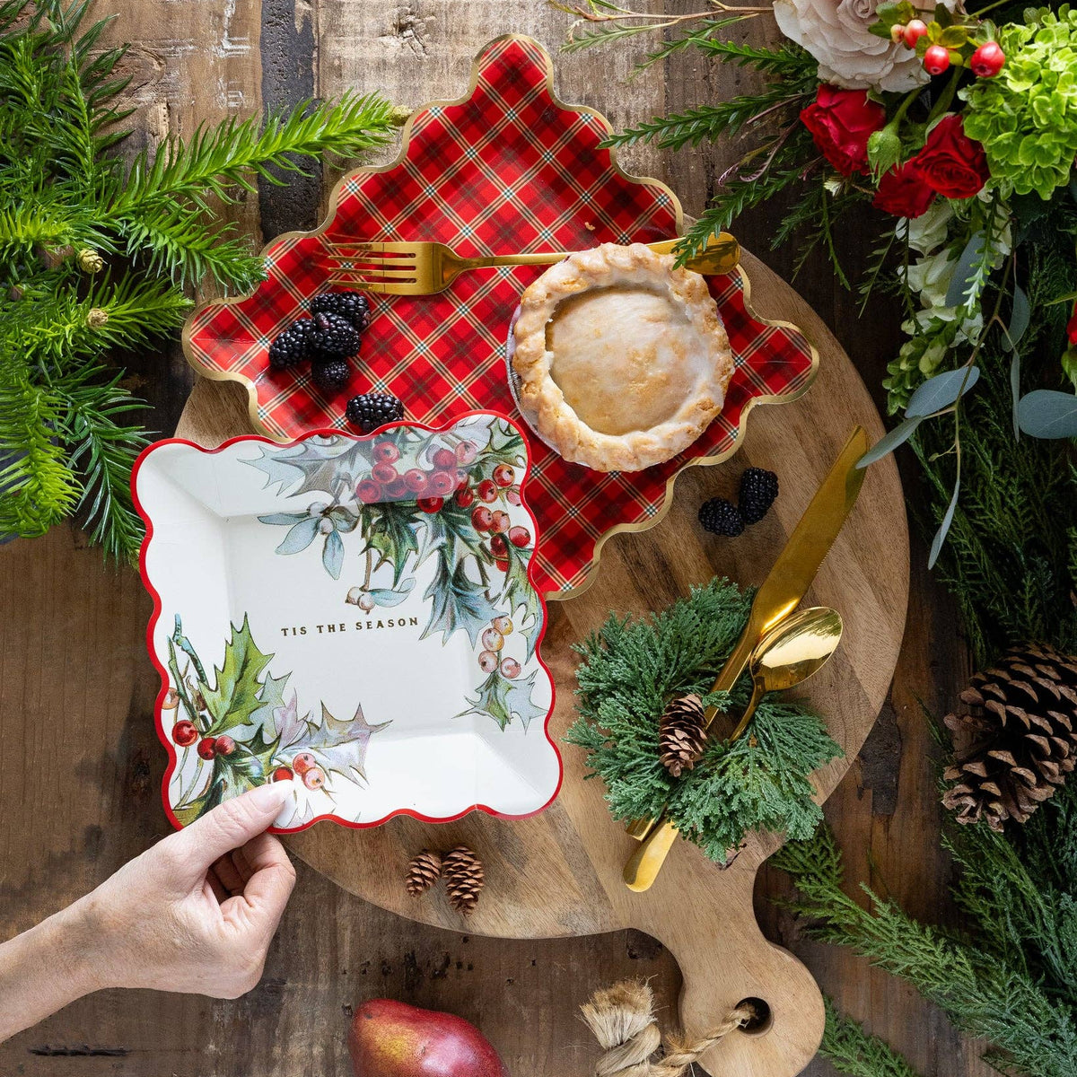 Holiday table setup with red plaid plate under holly plate on rustic wood board