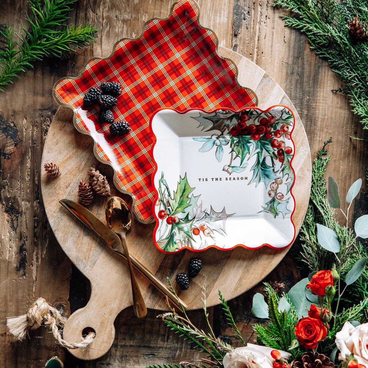 Festive table spread with holly plate and plaid plate surrounded by greenery