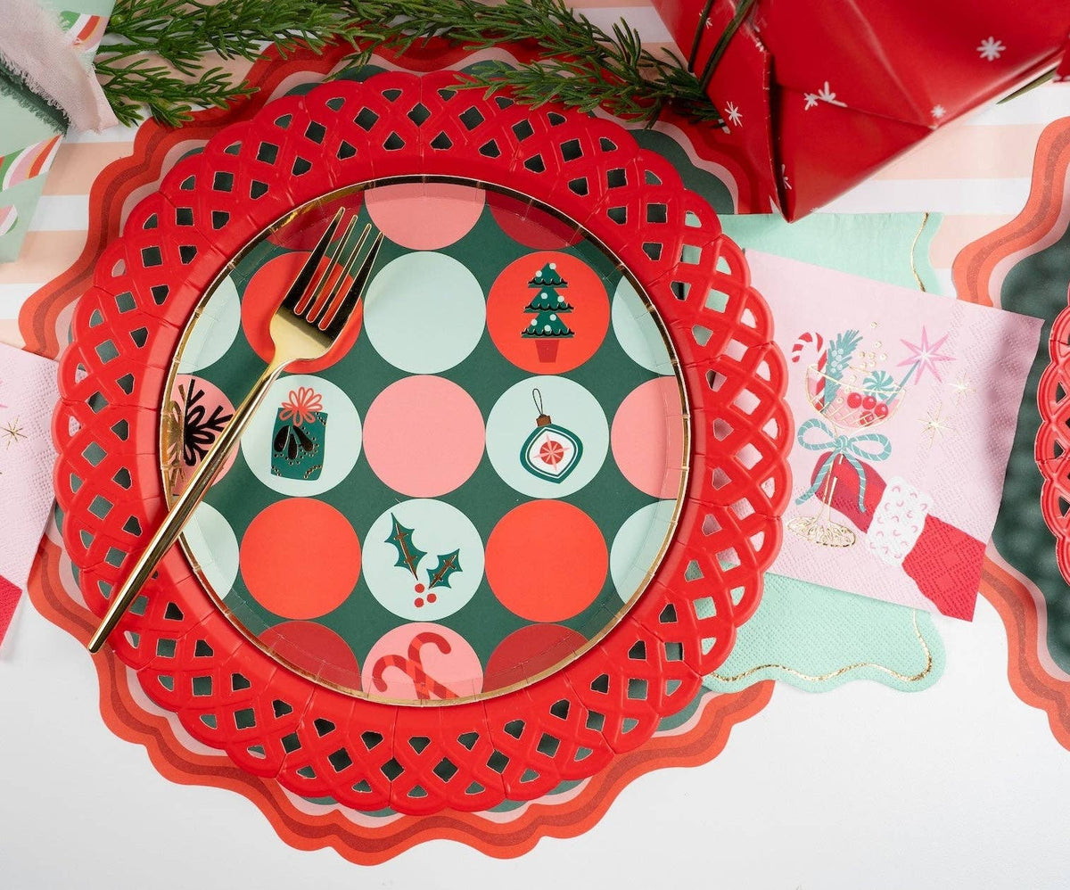 Overhead place setting featuring a red scalloped paper charger, a retro green and red dot pattern plate, and a gold fork.