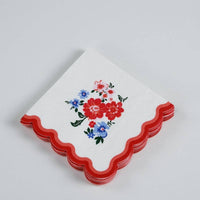 Stack of white cocktail napkins with red wavy scalloped borders and blue and red floral centers.