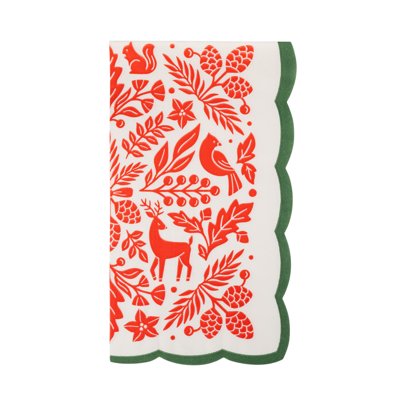 Cream paper dinner napkin with a red folk art print of a cardinal, deer, squirrel, pinecones, and poinsettias and a green scalloped edge