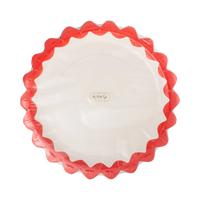 Cream paper plate with a red zig-zag edge shown at a slight angle.