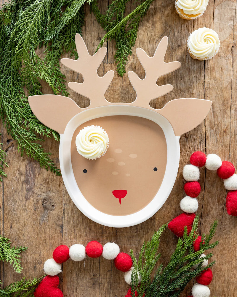 Overhead view of the reindeer serving tray on a wood table, decorated with pine and cupcakes, functioning as a beautiful Christmas platter.