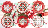 Wide overhead flat lay of a holiday table setting packed with red scalloped chargers, dot plates, pink napkins, and small wrapped presents.