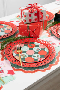 Angled view of a retro dot pattern holiday plate on a red scalloped charger set next to red and white polka dot wrapped gifts.