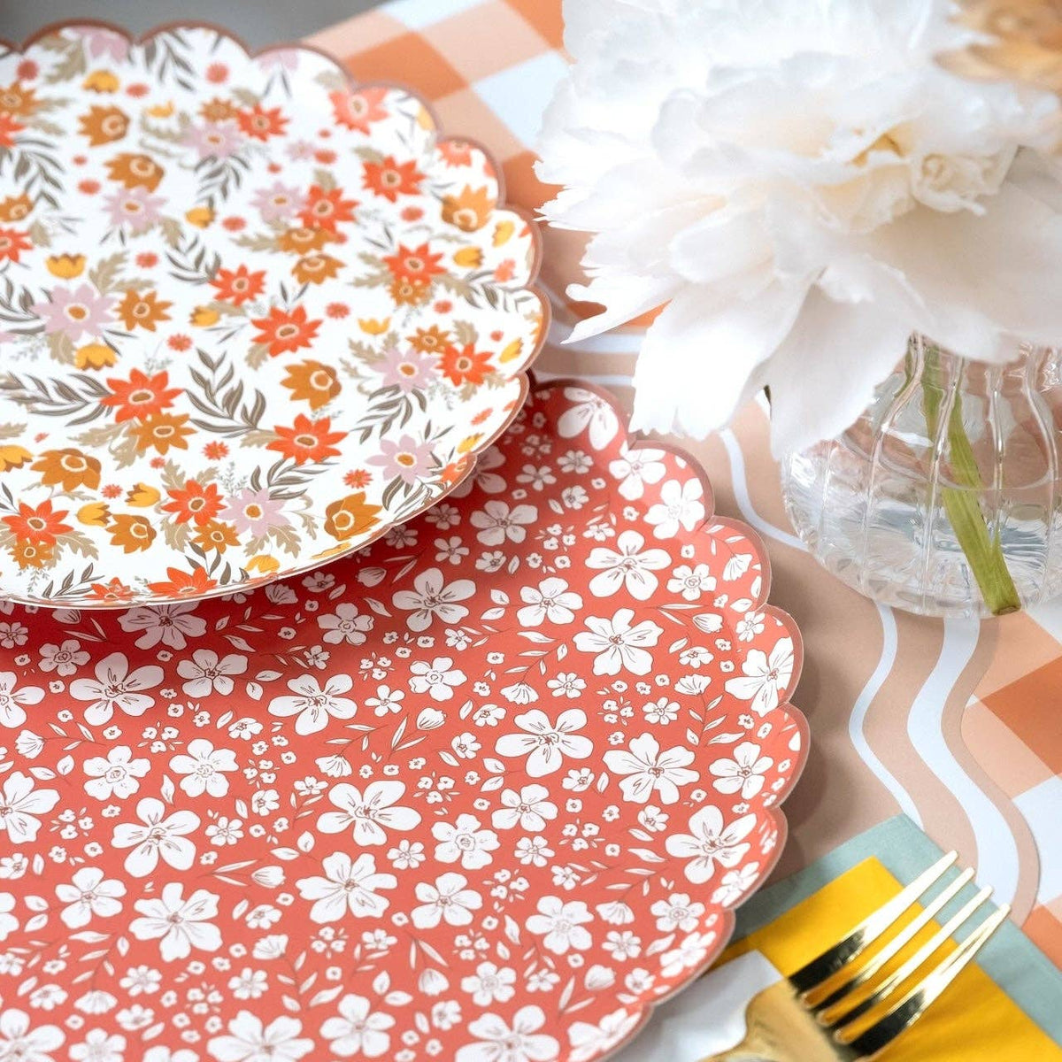 Cream fall floral plate resting on a rust floral plate beside a peony in a ribbed vase