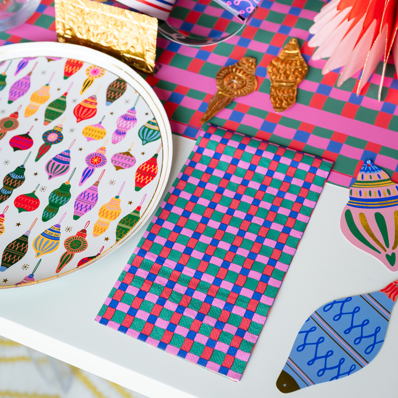 Styled holiday tablescape showing the checkered paper napkin layered next to a plate decorated with colorful retro Christmas ornaments.