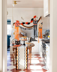 Halloween-themed kitchen with decorative pumpkins and 'Happy Halloween' banner along the ric rac table runner