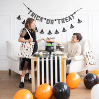 Two children decorating a table with a glow-in-the-dark ‘TRICK OR TREAT’ felt halloween banner and orange-black party setup