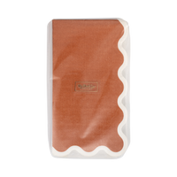 Stack of folded rust paper dinner napkins showing the solid color and cream wavy edge, front view.