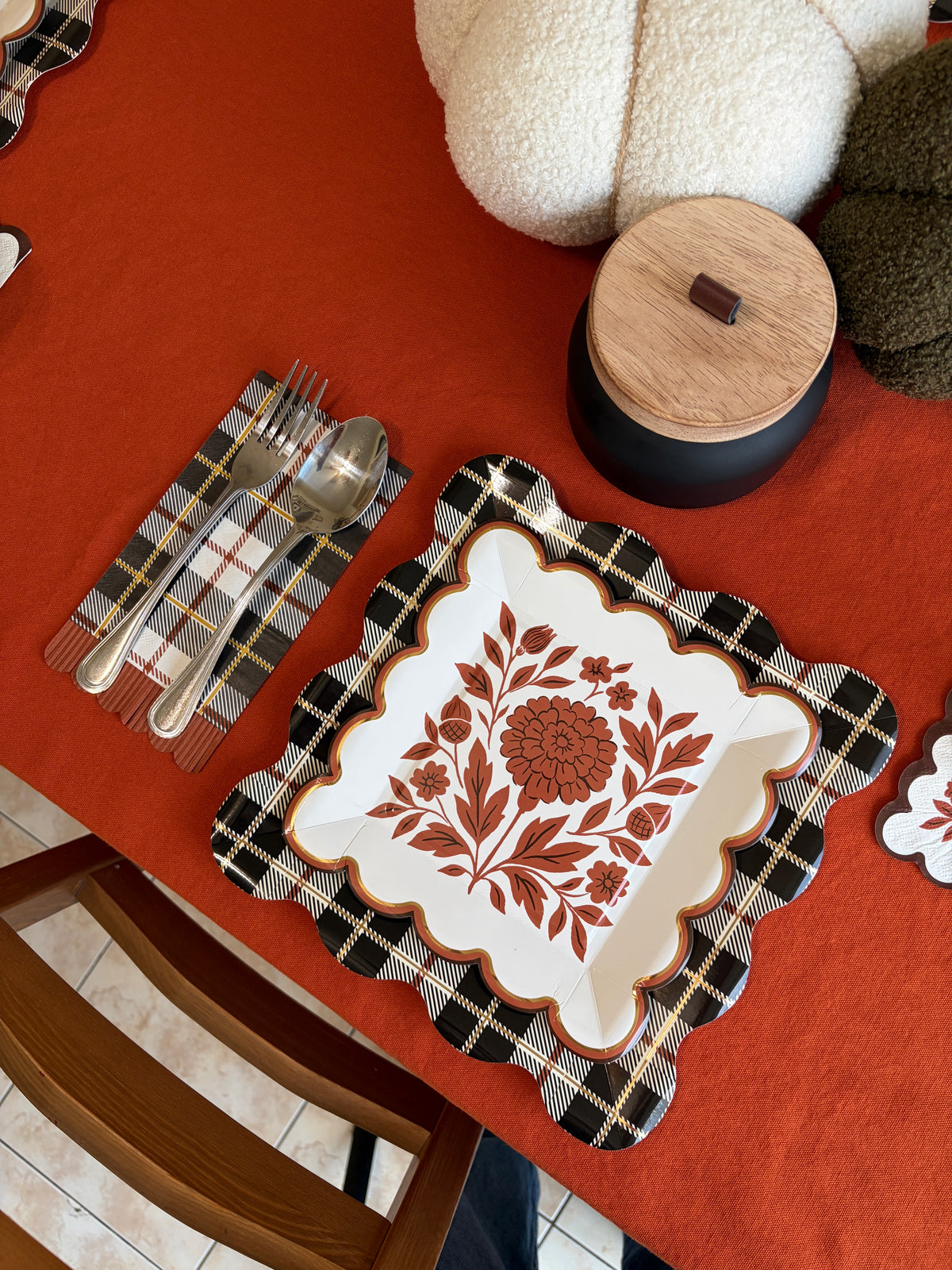 Overhead fall tablescape corner with rust folk floral square paper plates on plaid placemats, knit pumpkins, and an orange tablecloth