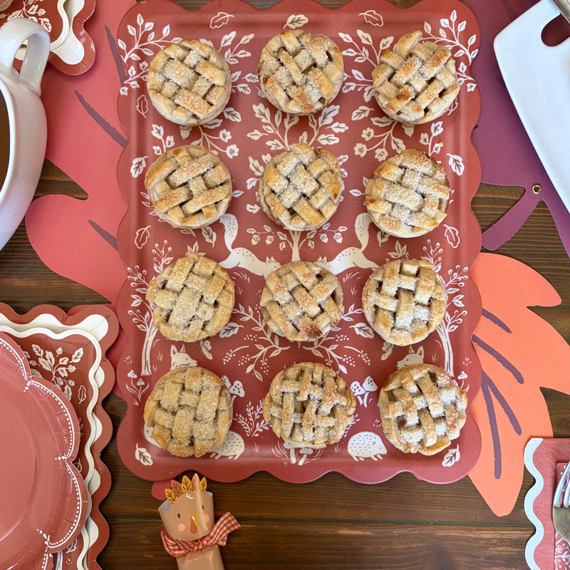 Rust scalloped serving tray with white squirrel, fox, hedgehog and mushroom print holding twelve mini lattice apple pies