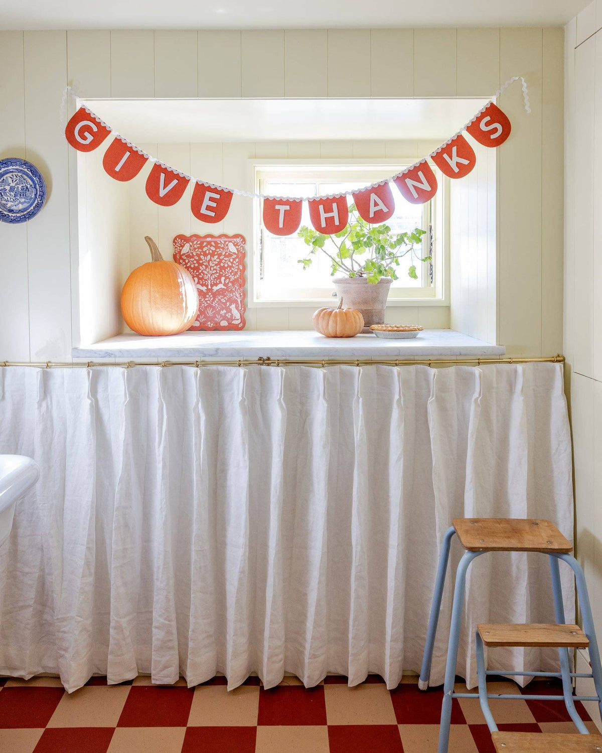 Thanksgiving orange felt banner draped elegantly below a bright window with autumn pumpkins resting on the sill.