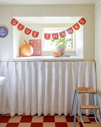 Thanksgiving orange felt banner draped elegantly below a bright window with autumn pumpkins resting on the sill.