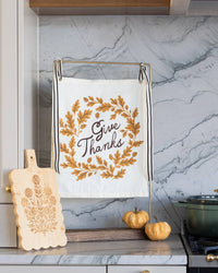 Wide lifestyle shot of the autumn canvas banner anchored against a grey marble kitchen backsplash next to a carved wooden board.