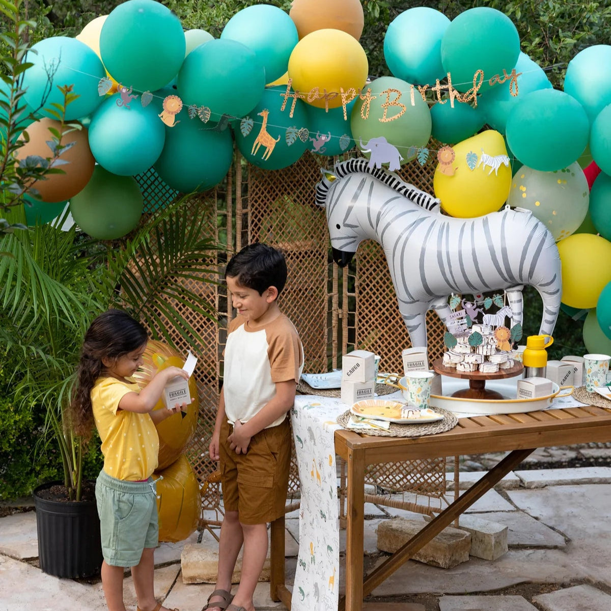 Outdoor safari theme party setup with zebra balloon and ‘happy birthday’ banner.