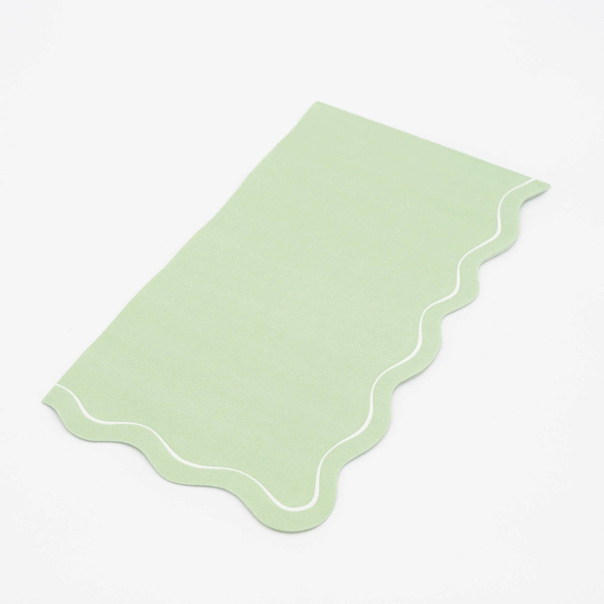 Folded sage green guest towel on a plain surface showing the muted green color and scalloped edge.