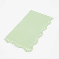 Folded sage green guest towel on a plain surface showing the muted green color and scalloped edge.