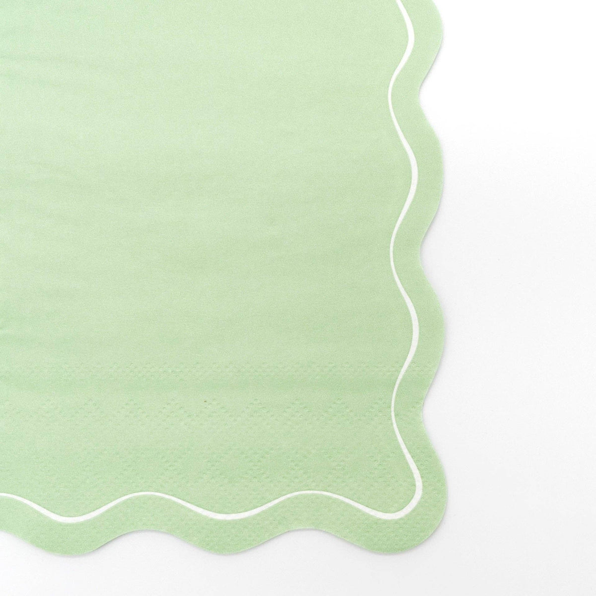 Close-up of the sage green paper guest towel showing the flowing scalloped edge and white outline detail.