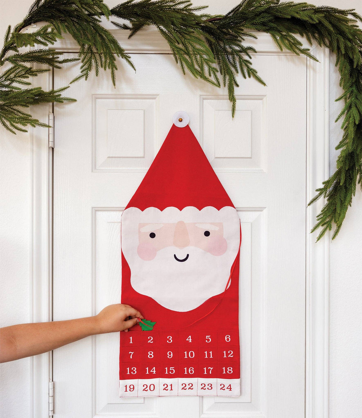 Santa canvas advent calendar hung on a white door with a hand reaching for a numbered pocket