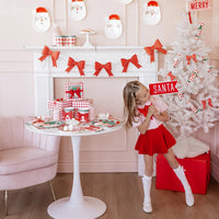hild holding Santa felt pennant next to a white Christmas tree—cute Christmas party props.