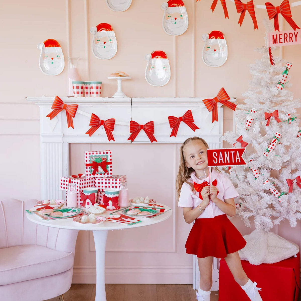 Girl posing with Santa felt pennant in a pink-and-red Christmas setup.