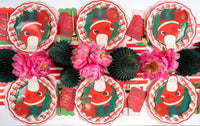 Overhead of Santa plates and red gift-card napkins on plaid plates around pink peonies and fringe trees.