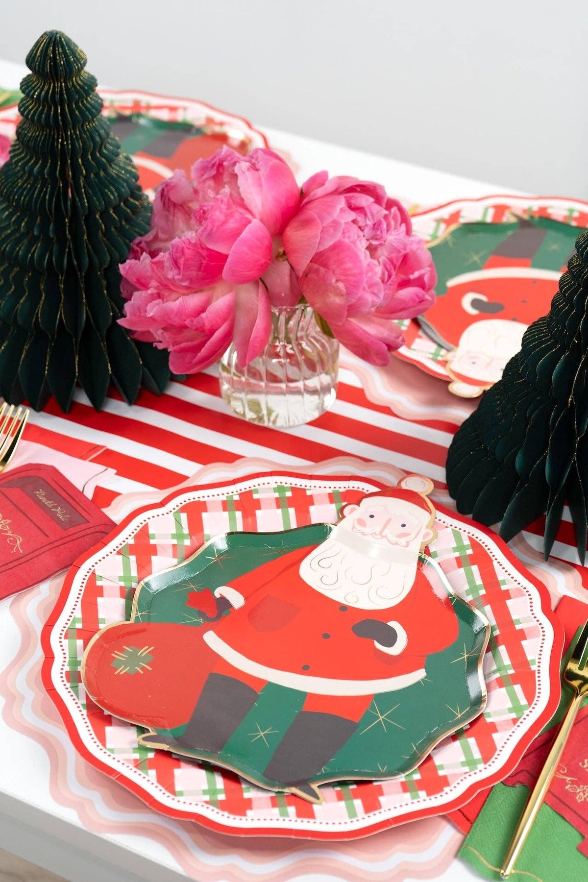 Overhead of Santa plates on plaid plates with pink peonies and black fringe trees.