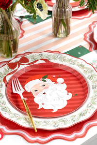 Place setting with the Santa dessert plate on a wreath plate, a pink-striped runner, and a gold fork.