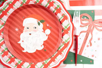 Place setting with the Santa dessert plate on a wreath plate and red scalloped charger, holly, and a gold fork.