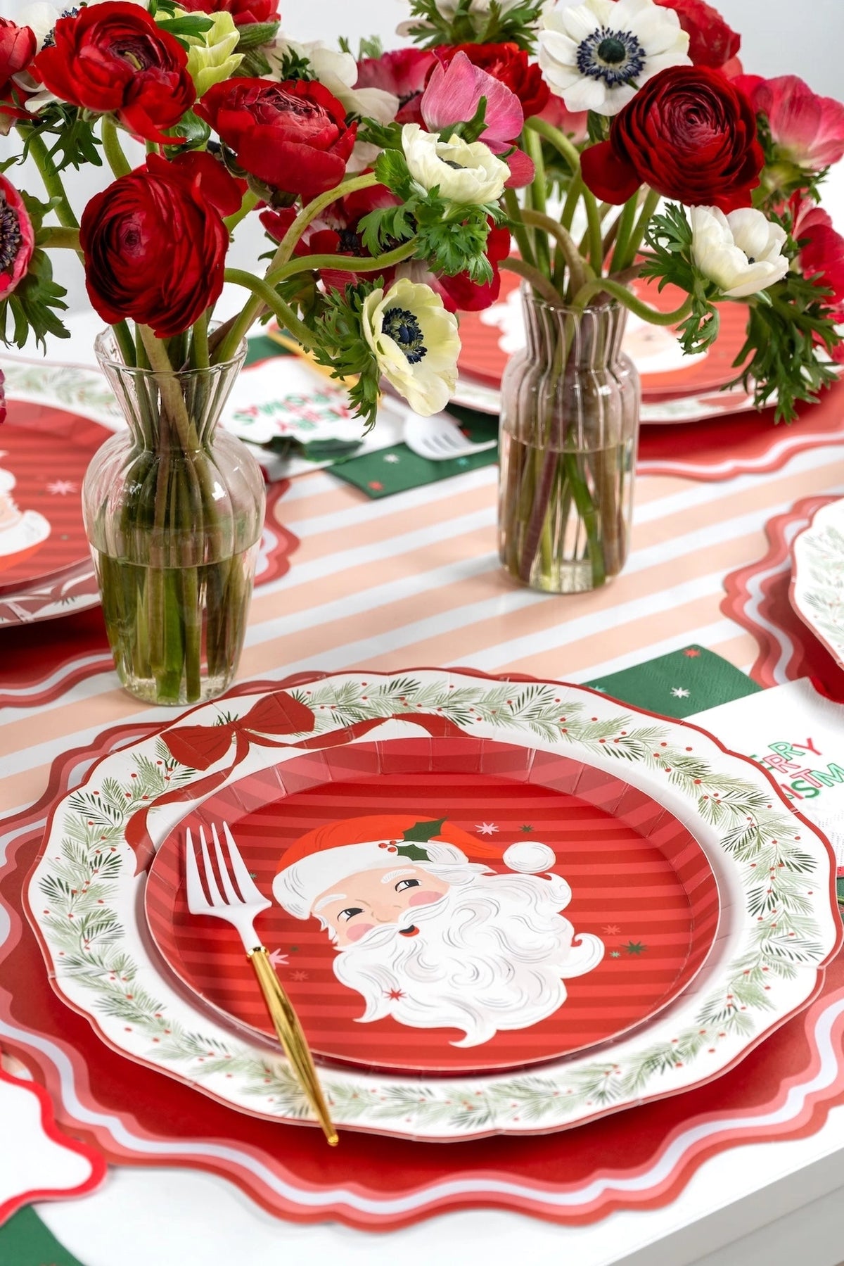 Place setting with a Santa plate on the wreath dinner plate, a pink-and-white striped runner, fresh flowers, and a gold fork.