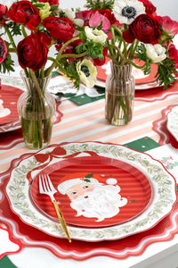 Place setting with a Santa plate on the wreath dinner plate, a pink-and-white striped runner, fresh flowers, and a gold fork.