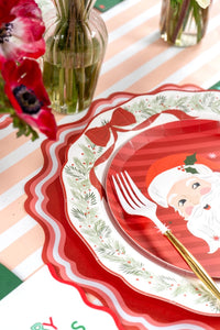 Place setting with a Santa plate on the wreath dinner plate, a striped runner, gold fork, and white anemones.