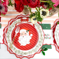 Place setting with a red-striped Santa salad plate on the wreath dinner plate and a red scalloped charger, with a gold fork and red anemones.