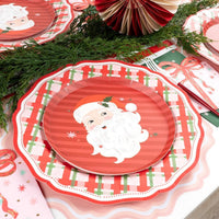 Place setting with the Santa dessert plate on a wreath dinner plate, a striped runner, evergreen, and a gold fork.